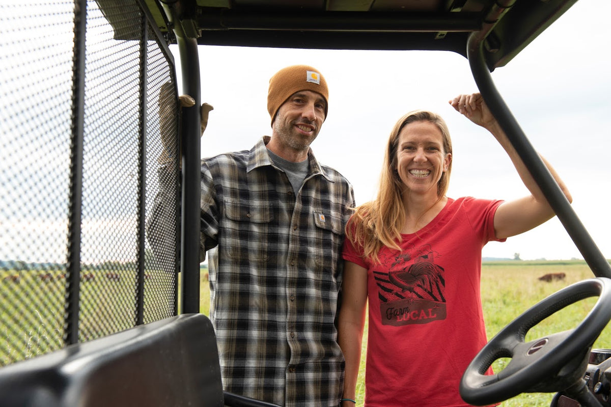 Bryce and Jen Riemer on the farm, with the herd grazing behind them